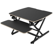 A flyyta 70 black standing desk converter with a plywood worktop and metal frame, designed for converting a traditional desk into a standing desk.