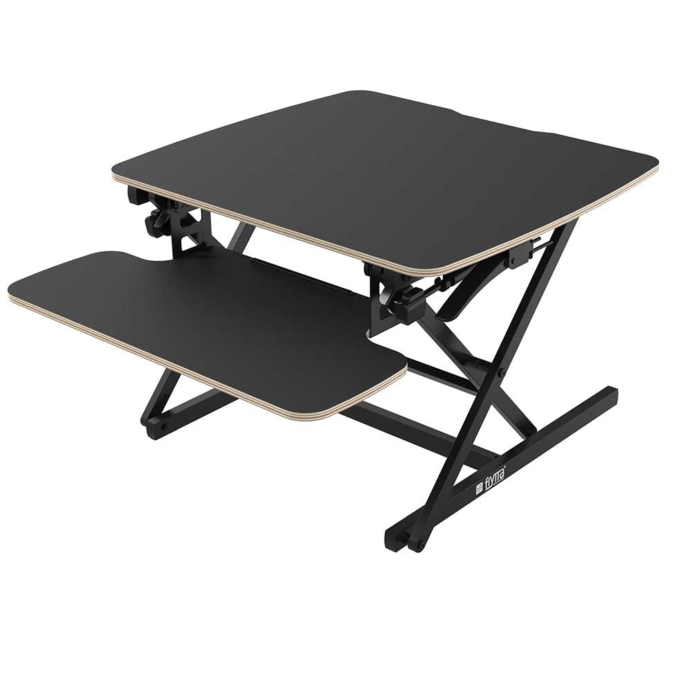 A flyyta 70 black standing desk converter with a plywood worktop and metal frame, designed for converting a traditional desk into a standing desk.